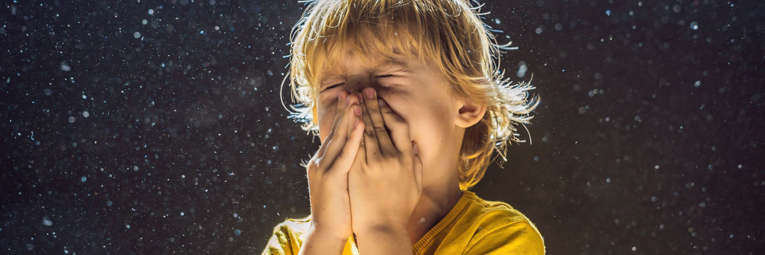 Allergy to dust. Boy sneezes because he is allergic to dust. Dust flies in the air backlit by light BANNER, LONG FORMAT