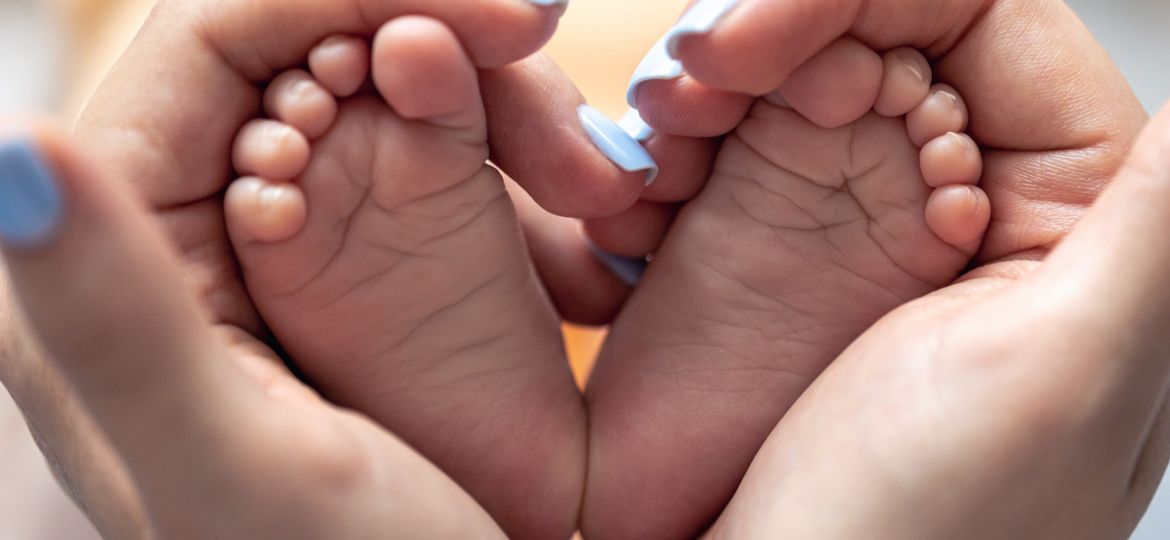 Mom holds the legs of a newborn baby in her hands.